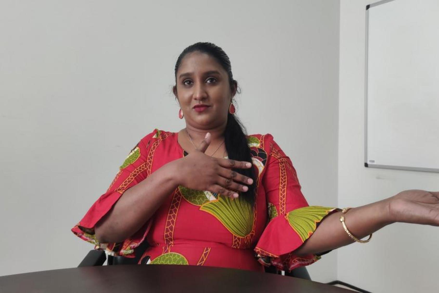 Una mujer con un vestido colorido se sienta en una mesa mientras mira directamente a la cámara.