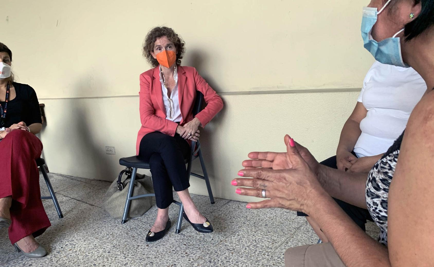 تجلس المنسقة المقيمة في الوسط مرتدية كمامة وهي تستمع إلى نساء يشاركن قصصهن.