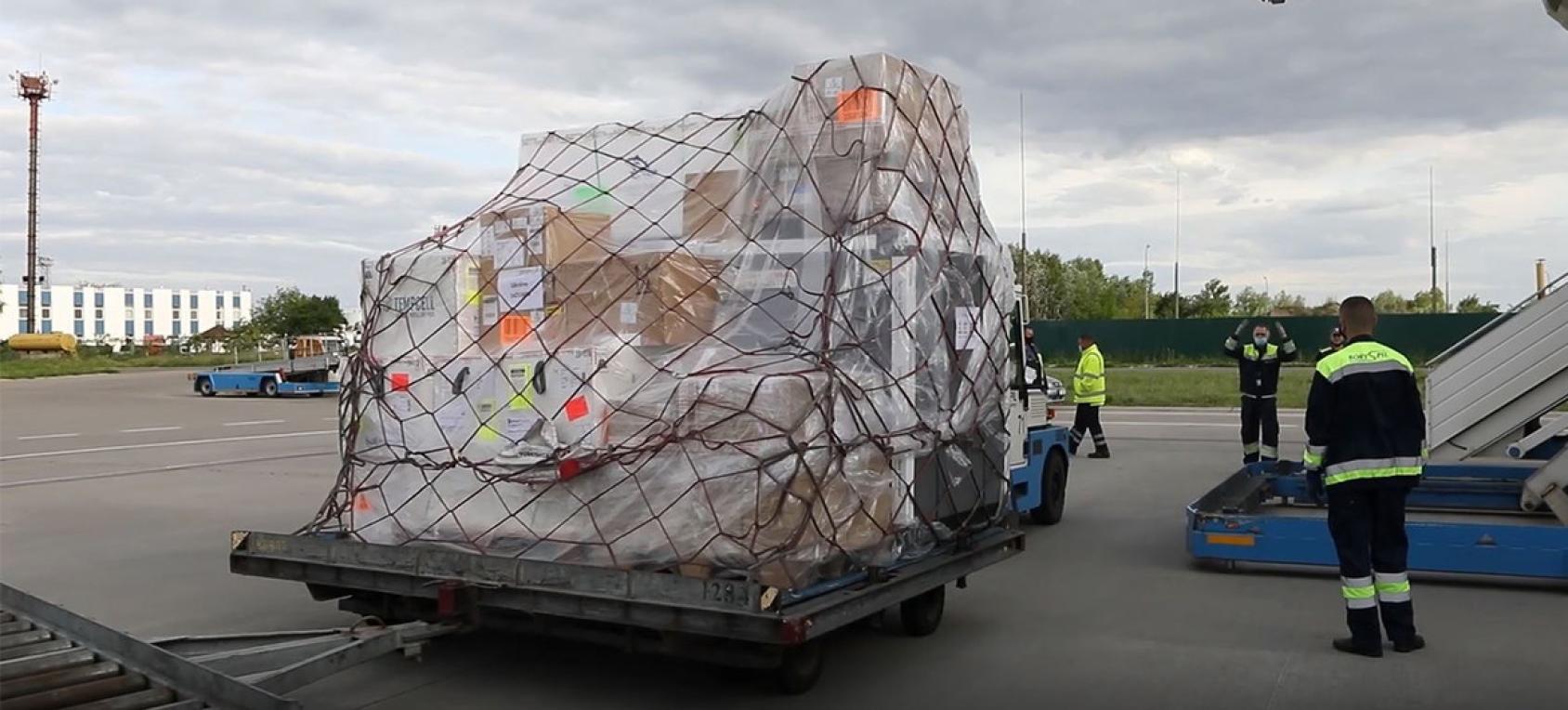 грузчики разгружают партию вакцин на летном поле.