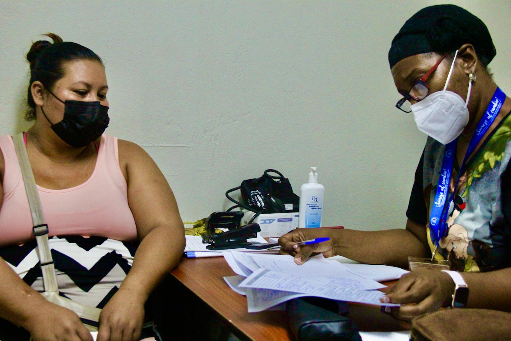 ممرضة تجلس على مكتبها وتتحدث مع مريضة.