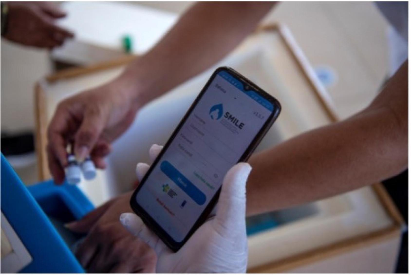 صورة لهاتف جوال يعرض تطبيق Smile، ويد مرتدية قفاز تمسك بالهاتف.
