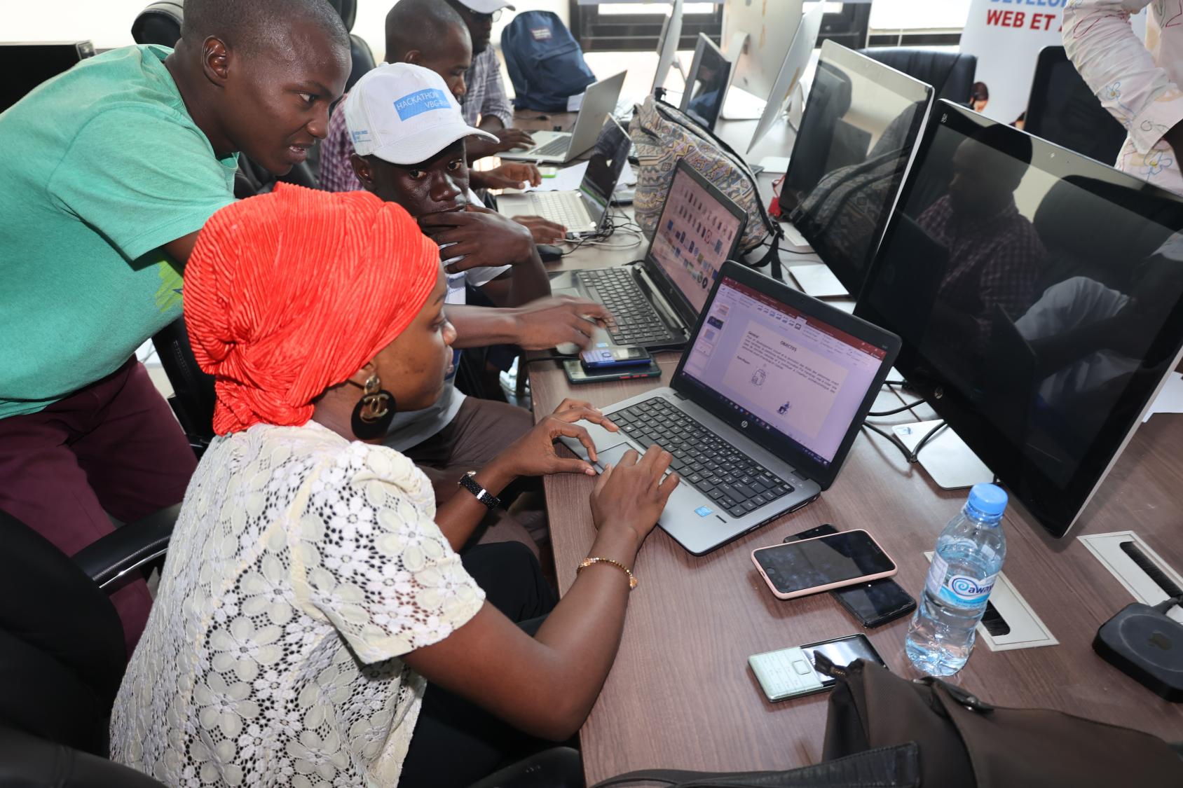 Dans une salle de formation, une jeune femme portant un fichu de couleur orange vif et deux jeunes hommes travaillent sur un ordinateur portable en discutant.