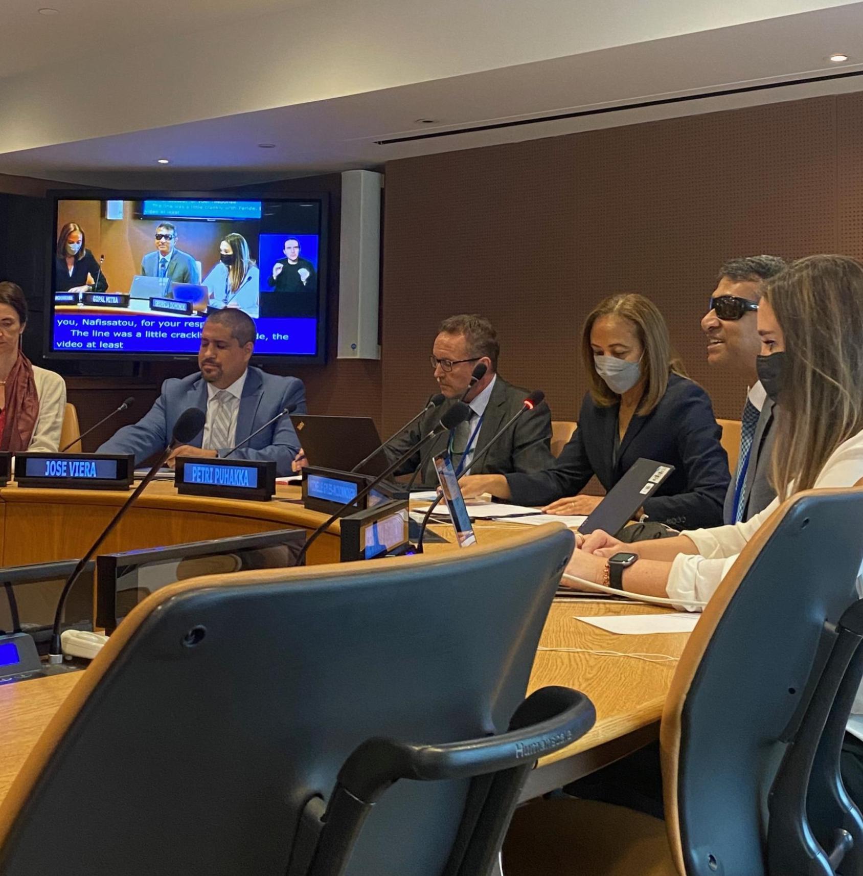 يجلس المتحدثون حول طاولة مستديرة ويناقشون جدول الأعمال مع شاشة خلفهم.