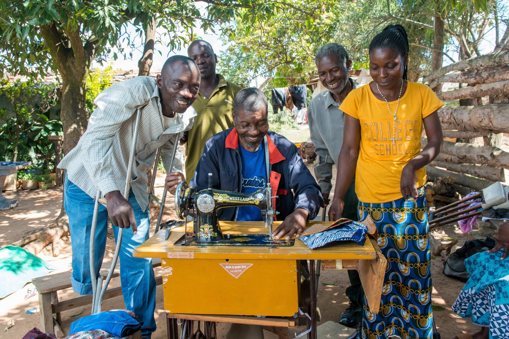 مجموعة من الأشخاص تقف حول رجل يعمل على ماكينة خياطة.