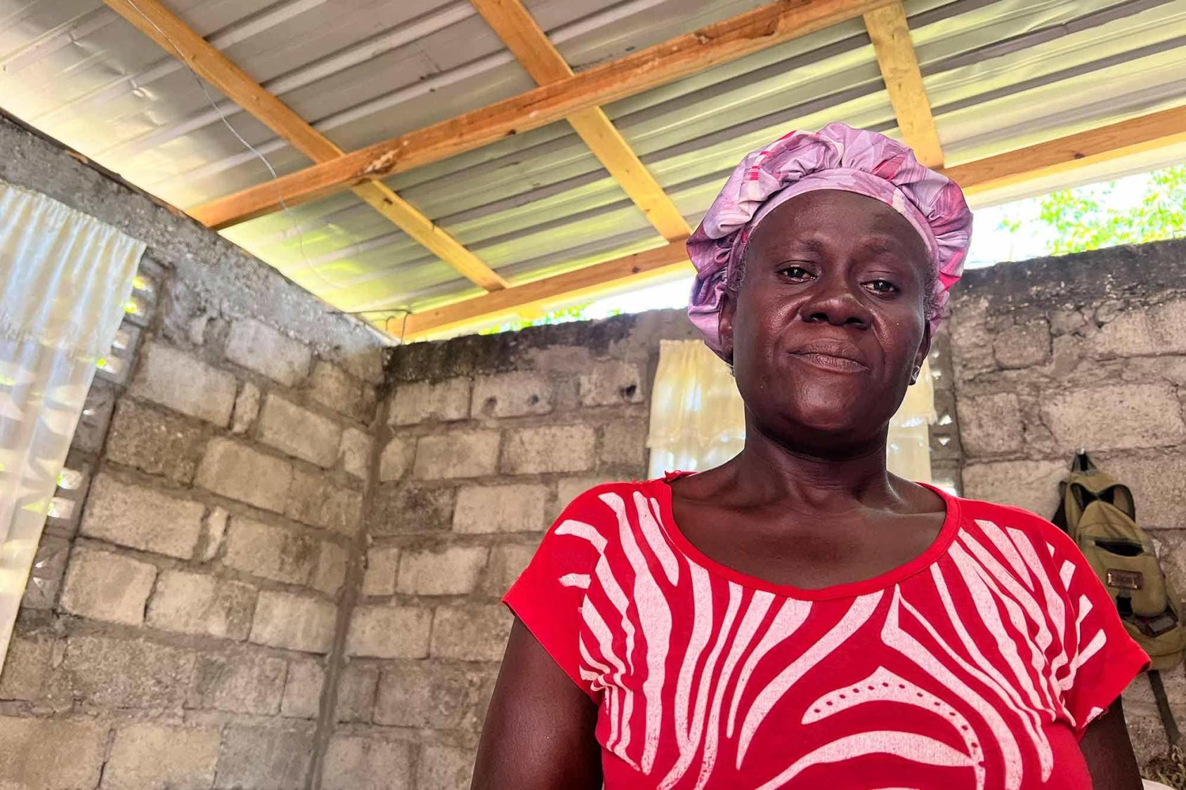 Retrato de una mujer en Haití con una blusa roja y de pie en una habitación protegida por un techo de hojalata.