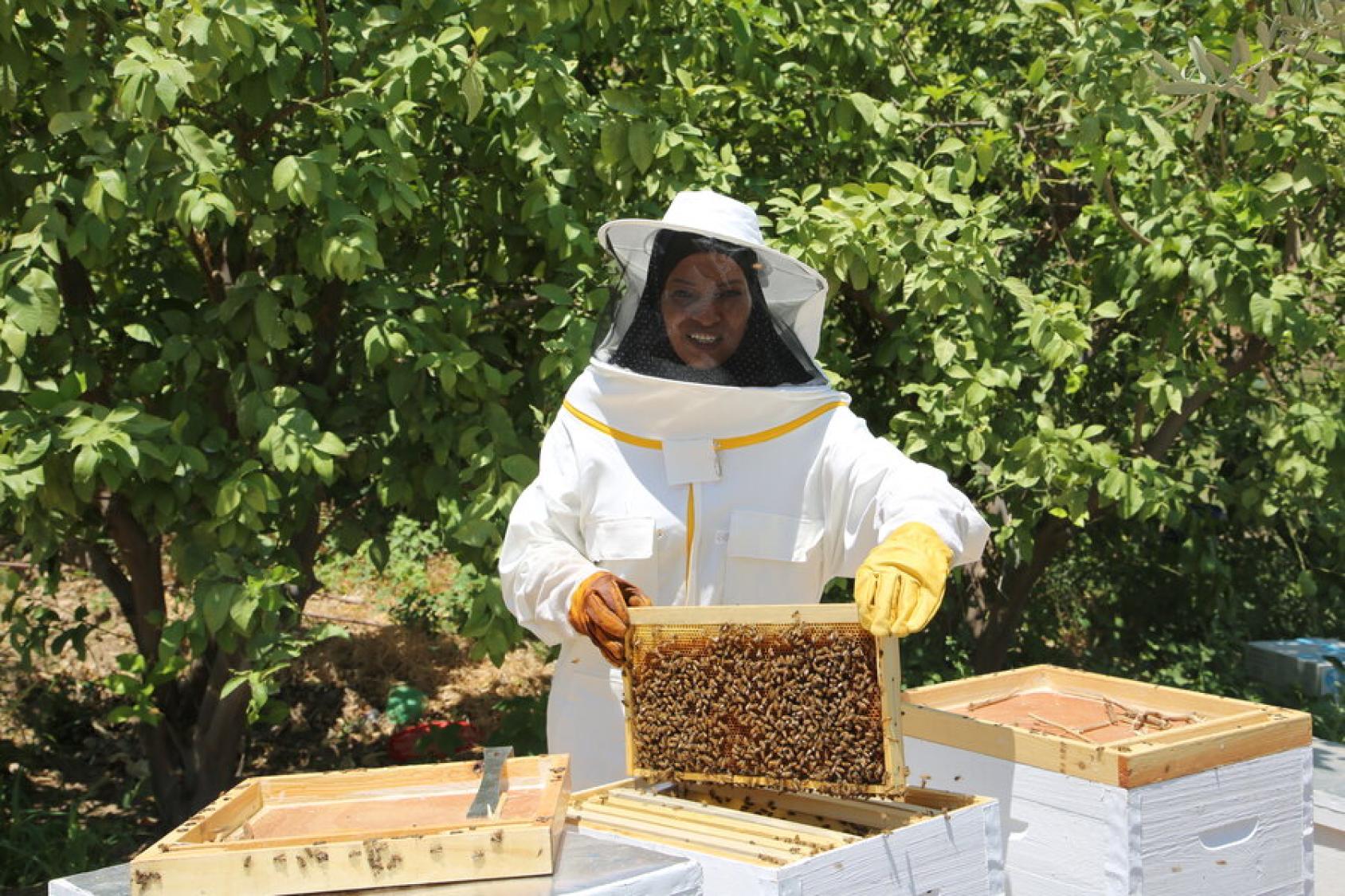 A woman beekeeper holds a hive of bees and looks into the camera for a photo.