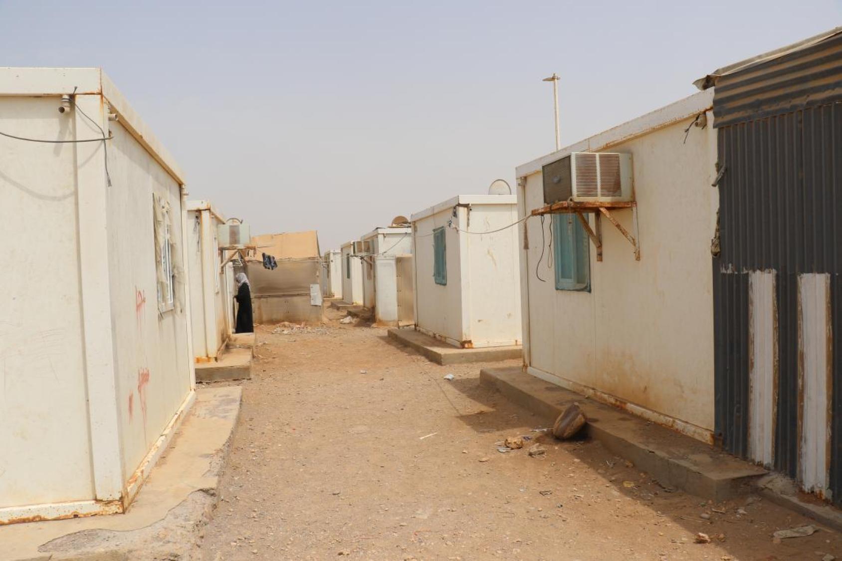 Vue d’une allée bordée par deux rangées d’abris pour réfugiés aux murs extérieurs blancs.