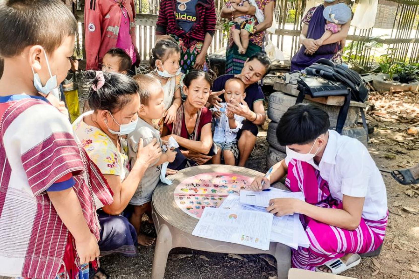 يجلس النساء والأطفال الصغار حول طاولة وينظرون إلى أحد الموظفين يملأ الاستمارات.