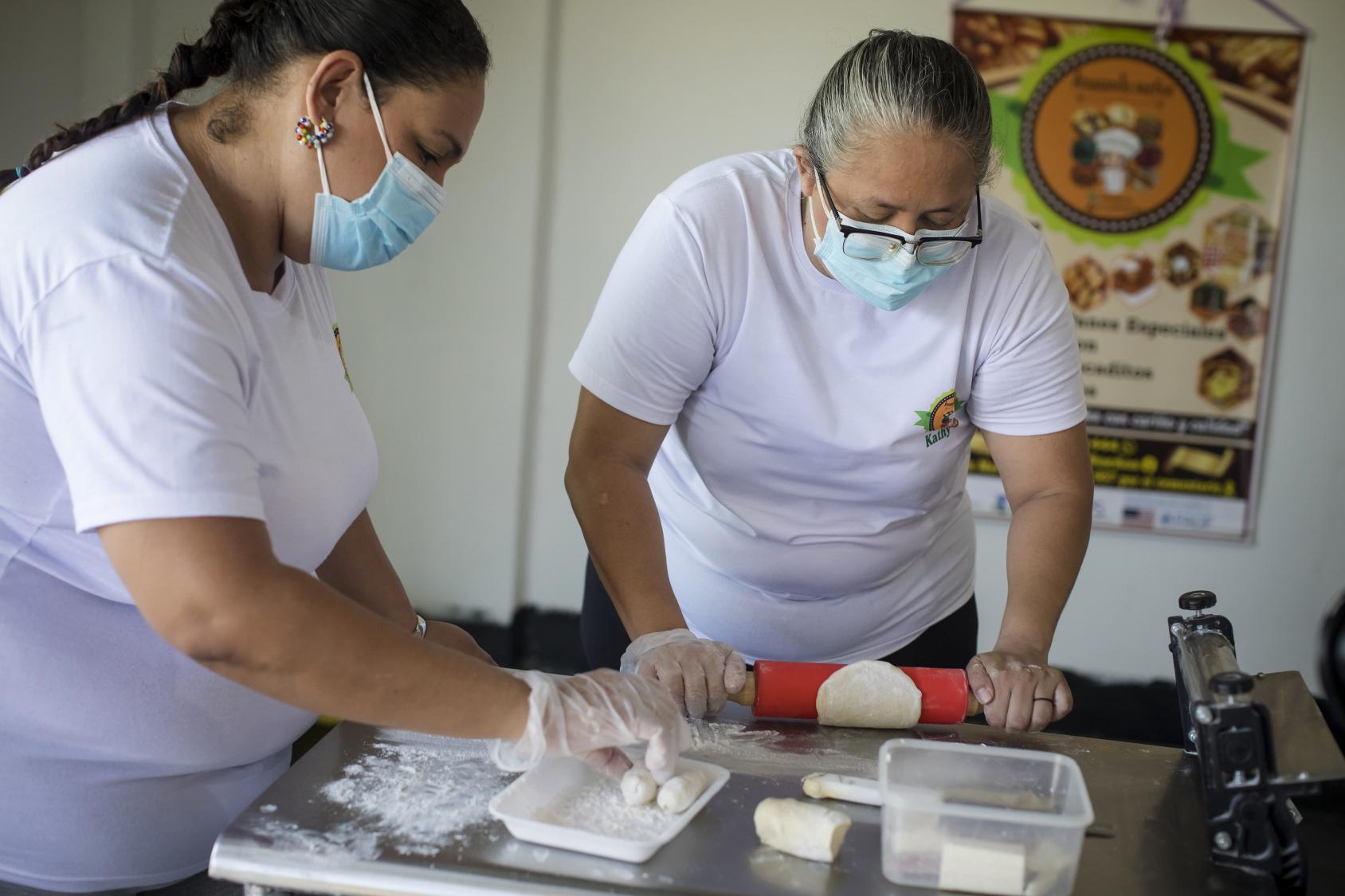 Two women in white shirts rolling bread in a kitchen