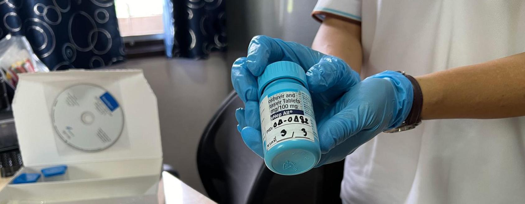 Two hands in blue gloves hold a bottle of medication in blue