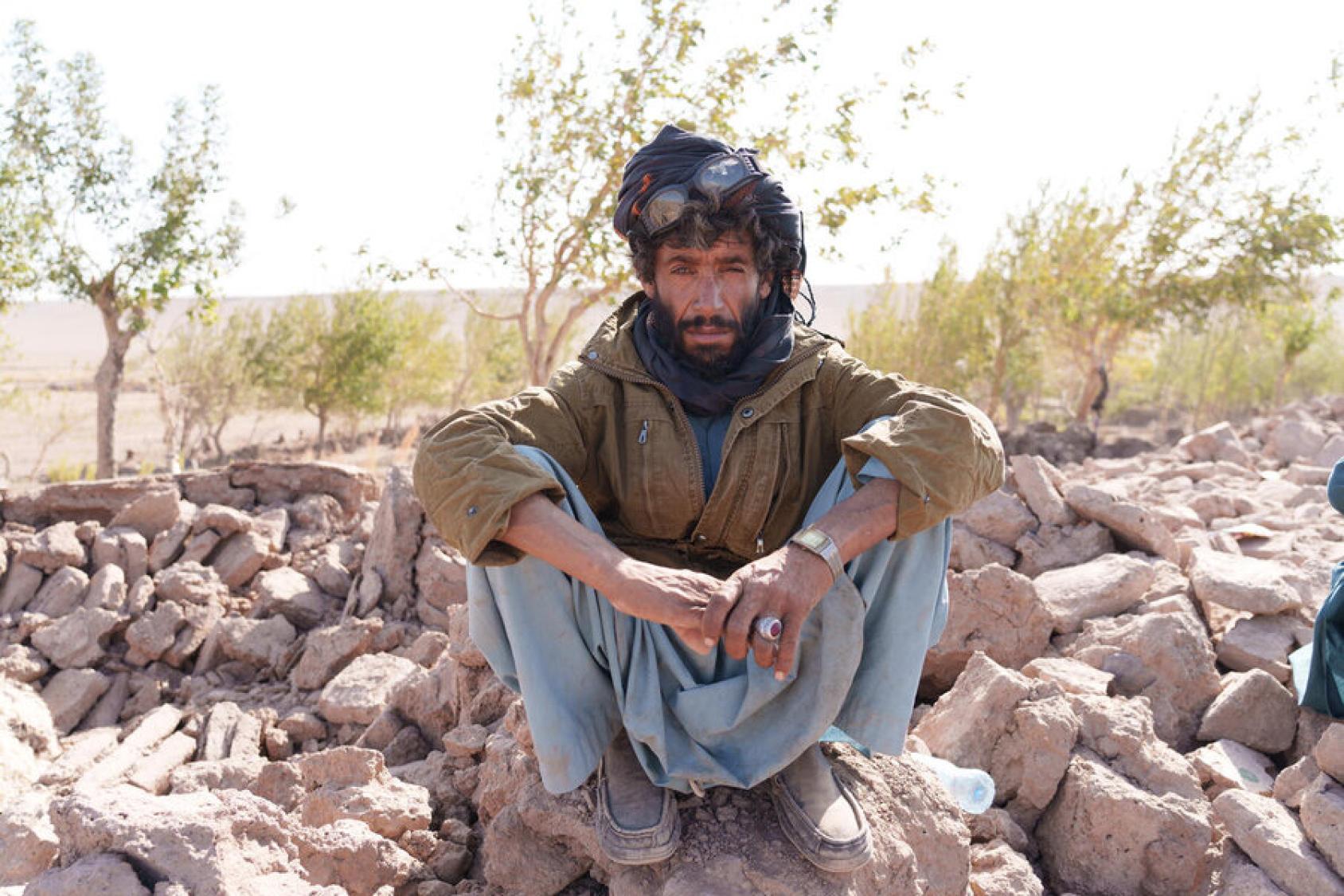 A shepherd, dressed in green and black, crouches among the rubble from the earthquake in Herat. Afghanistan