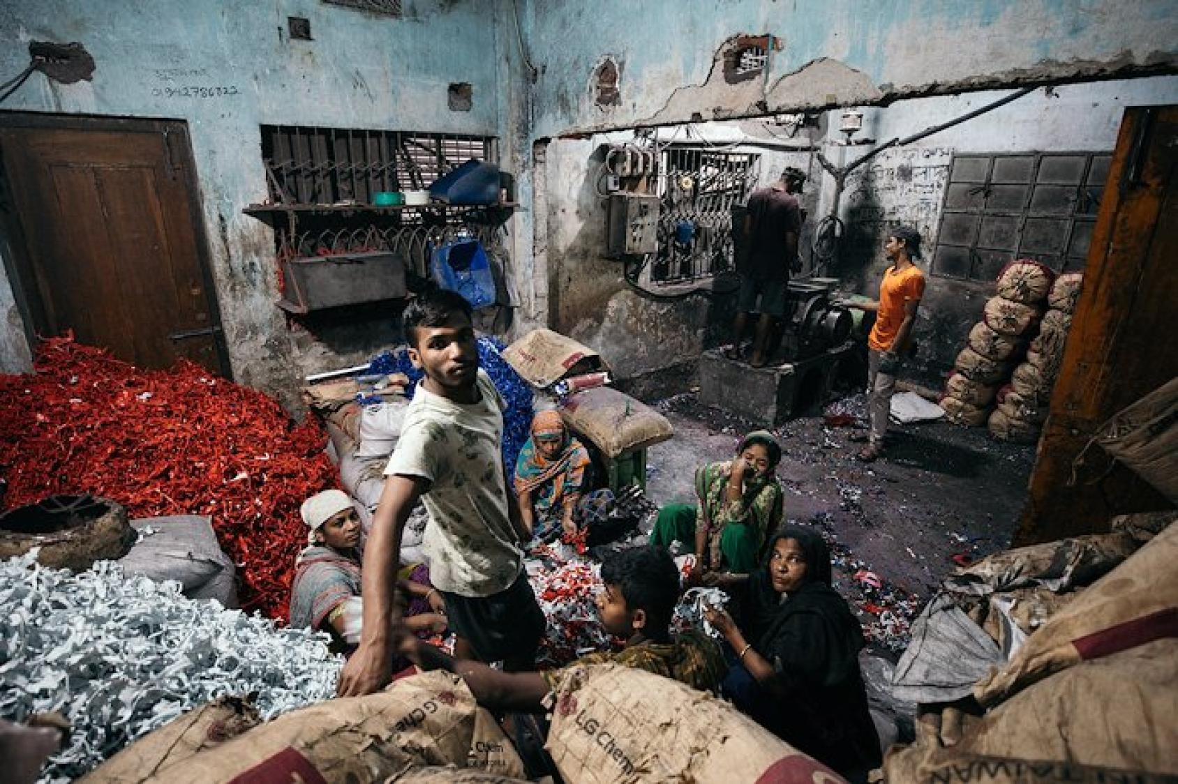Three people crouched over bags of wastepaper in a workshop