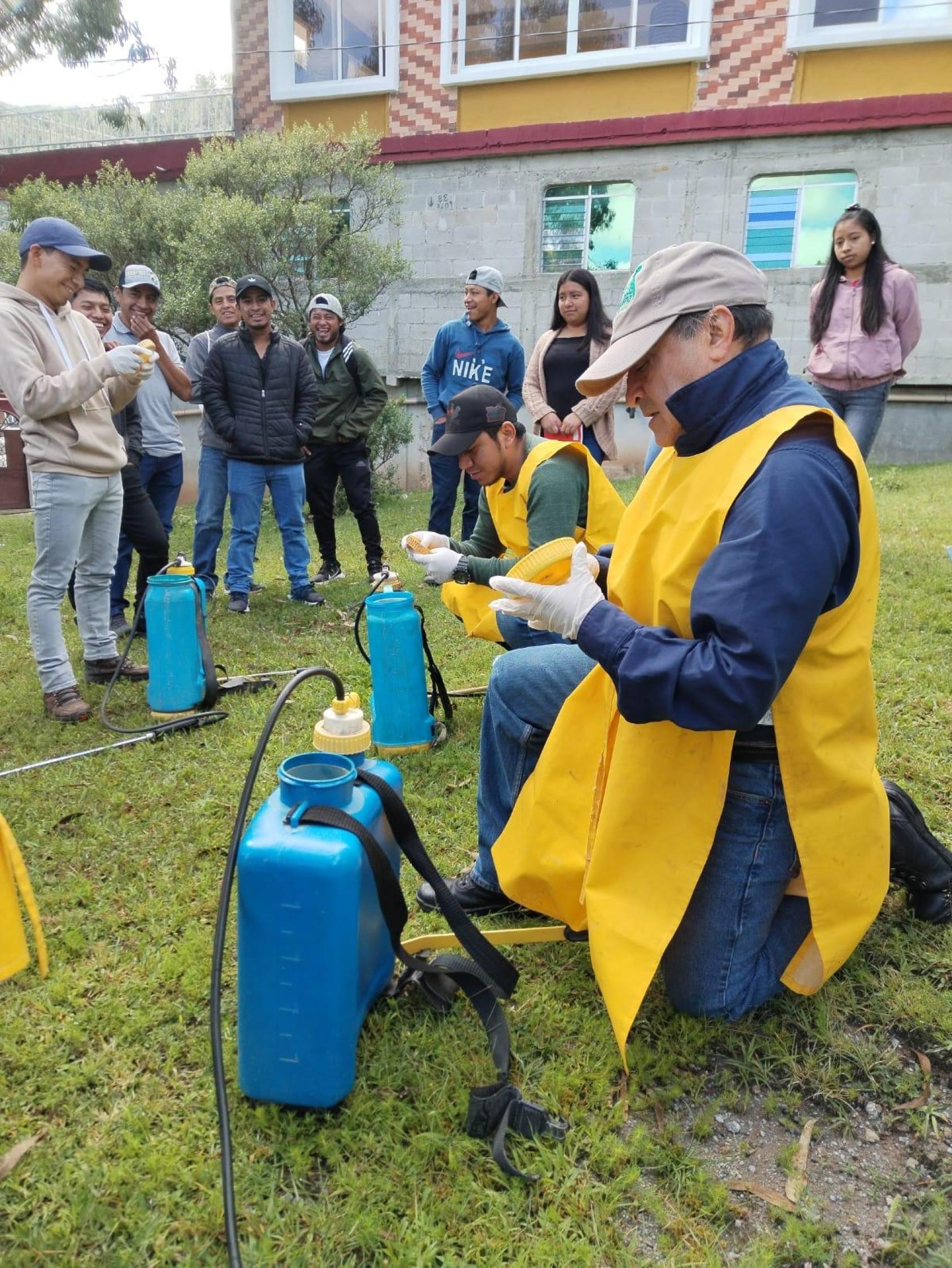 A man in a bright yellow vest shows a group how to dispose of chemical containers.