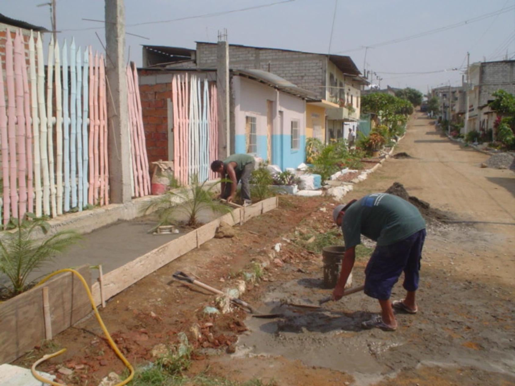 La gente planta plantas fuera de edificios coloridos en un camino de tierra.