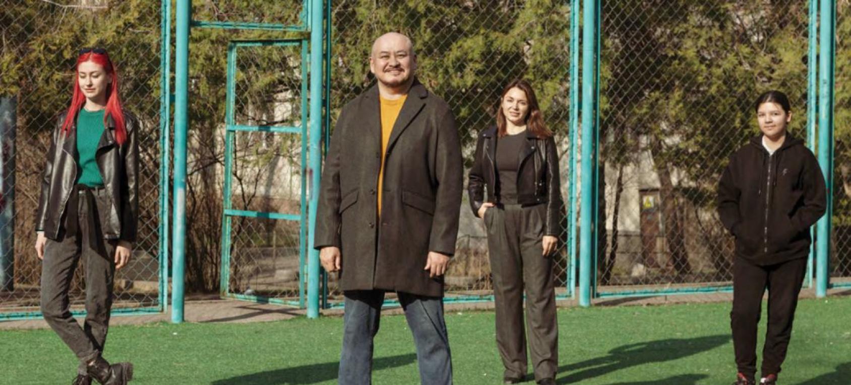 Молодые люди, три женщины и мужчина, позируют на спортивной площадке