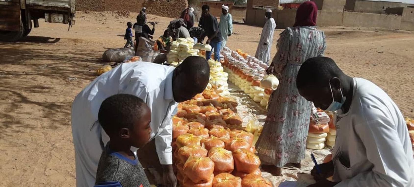 People being handed food outdoors, a man stands with a young child
