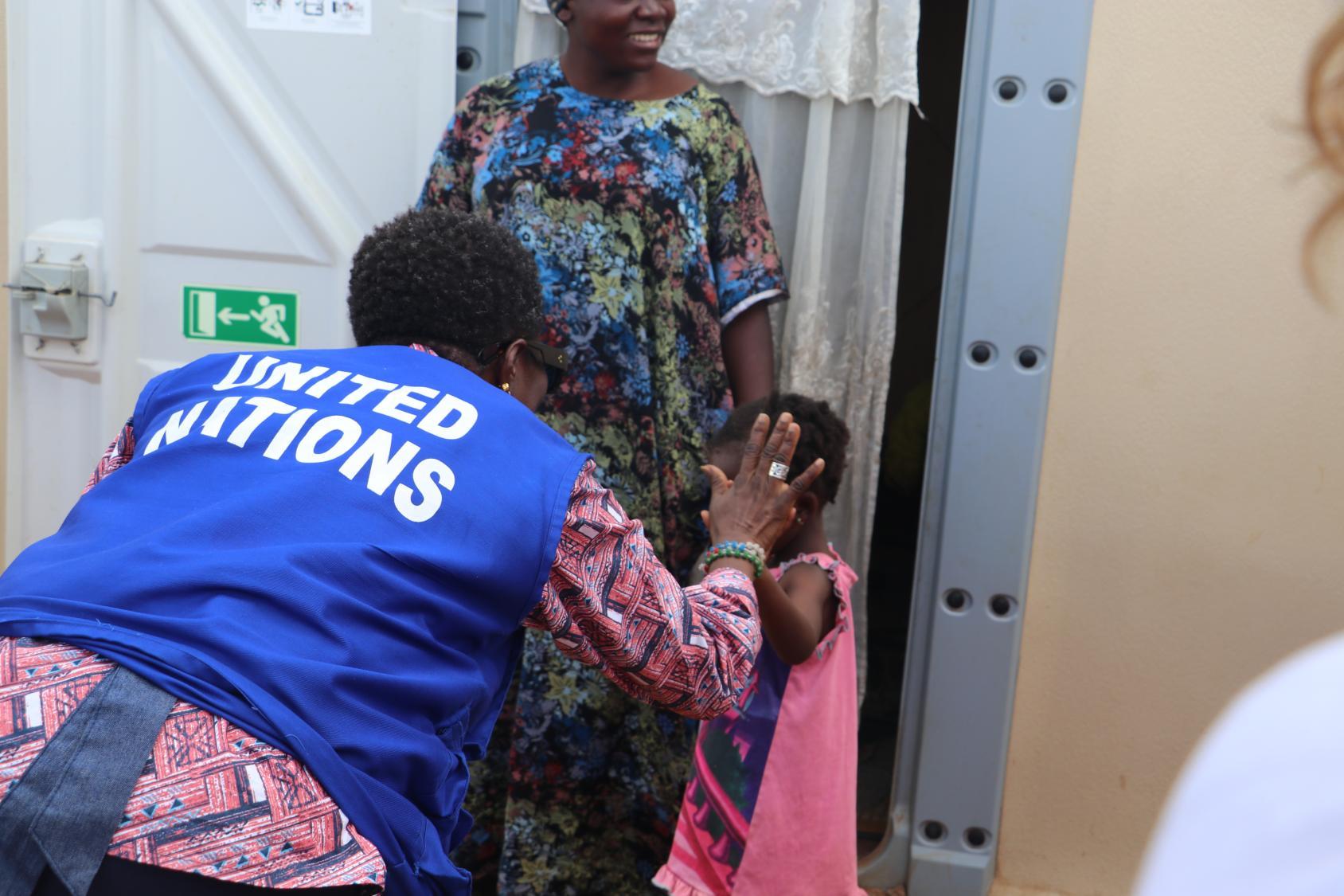 A woman in a pink dress and blue vest gives a high five to a child in a pink dress