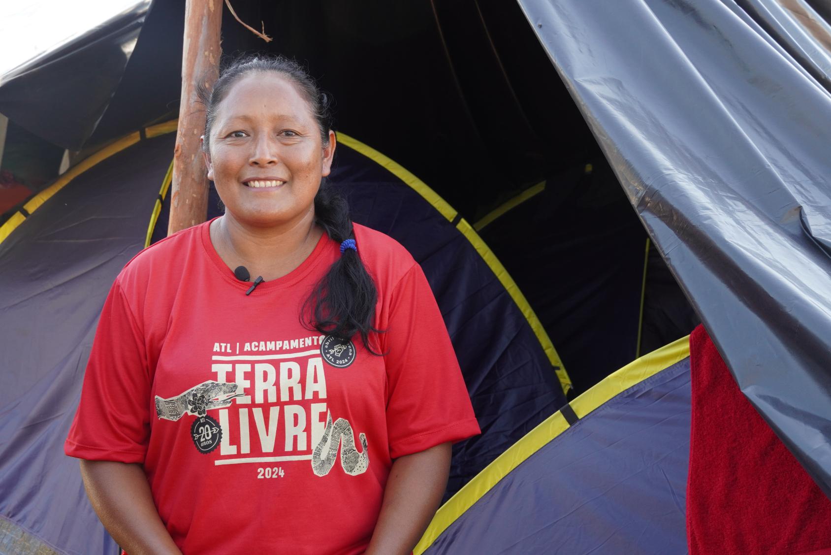 A woman in a red shirt stands in front a blue tent