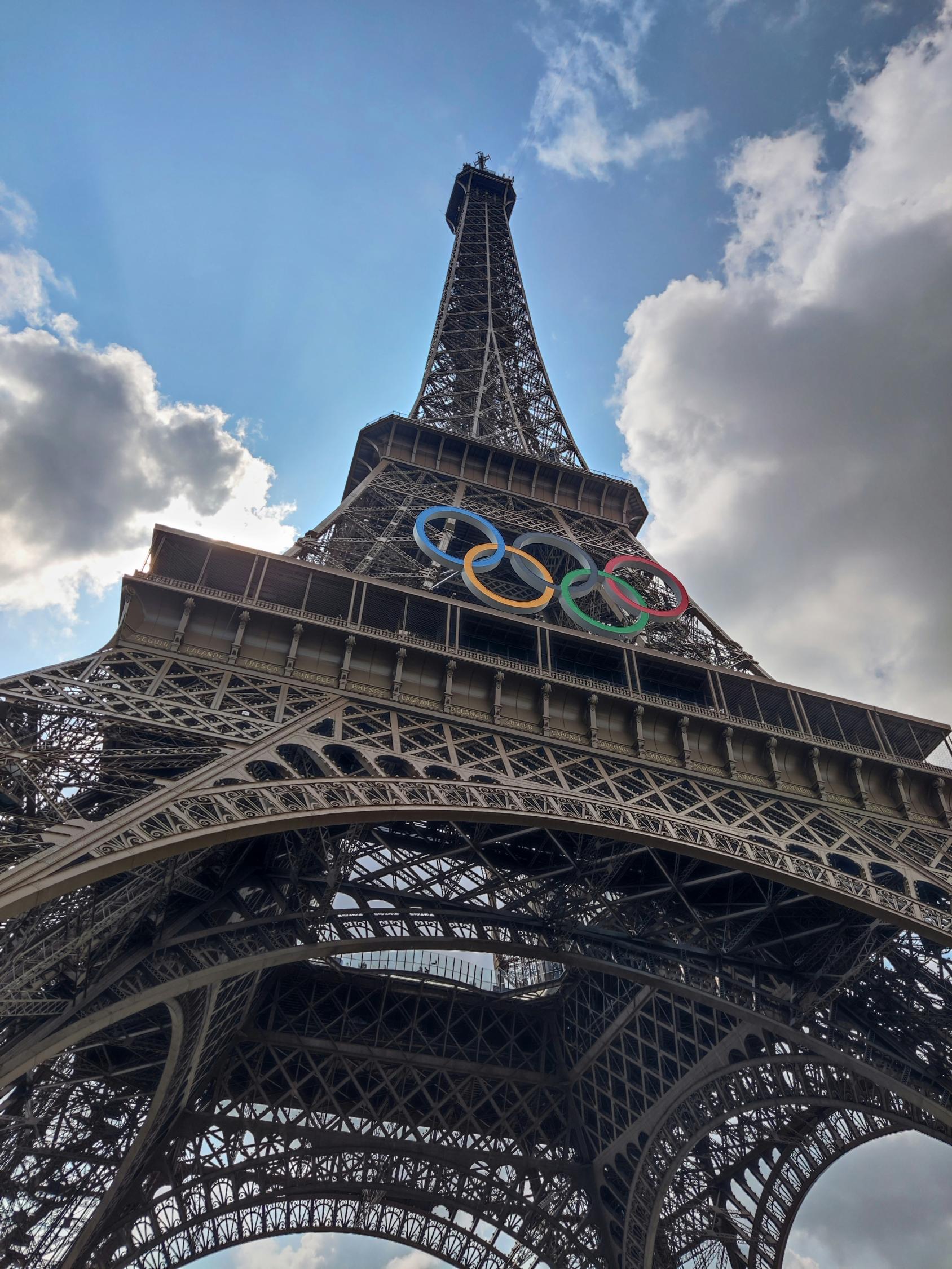 A short of the Eiffel tower with the Olympics rings hanging on the beams