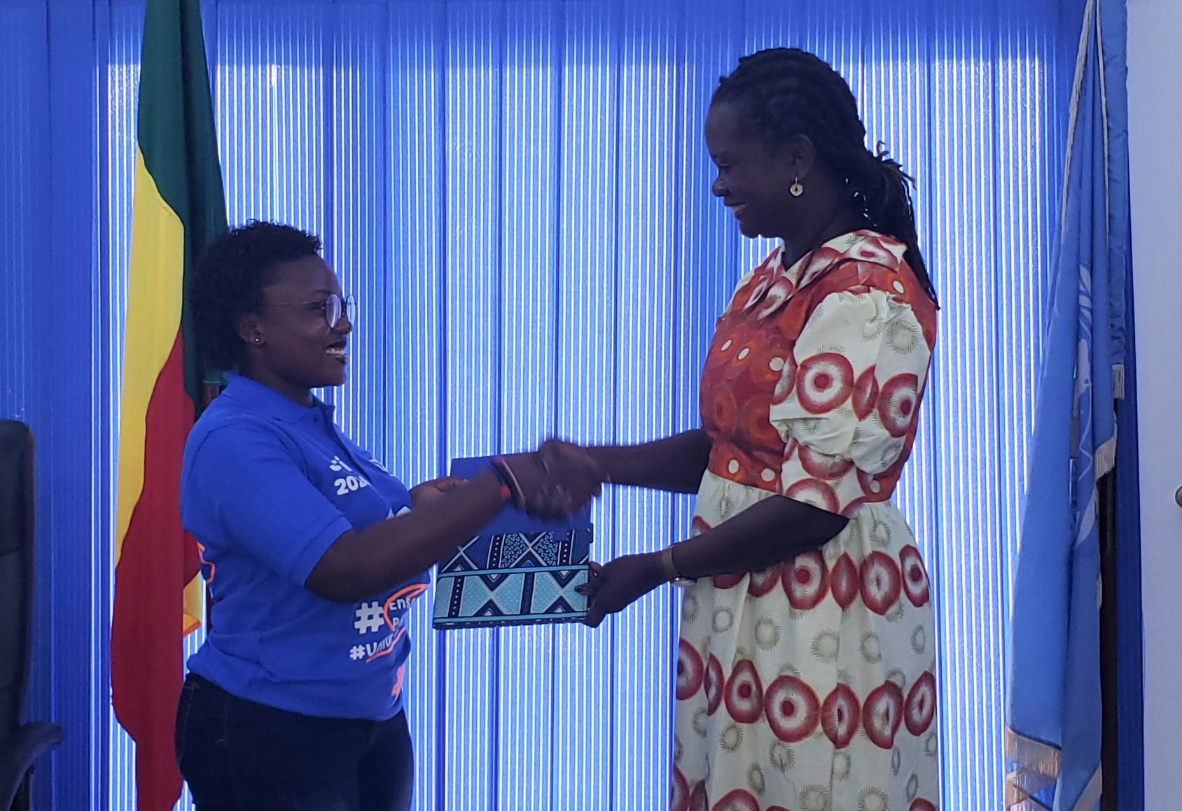 Anastasie Bankolé (à gauche) endosse le rôle de Coordonnatrice résidente des Nations Unies pour une journée, tandis qu'elle reçoit des documents de travail pour cette nouvelle fonction de la part d'Aminatou Sar (à droite), Coordonnatrice résidente des Nations Unies au Bénin. 