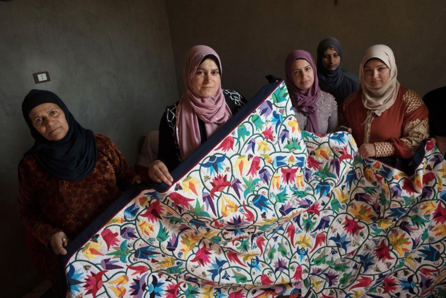 Five women dressed in dark clothes and headwear hold up a colourful piece of fabric.