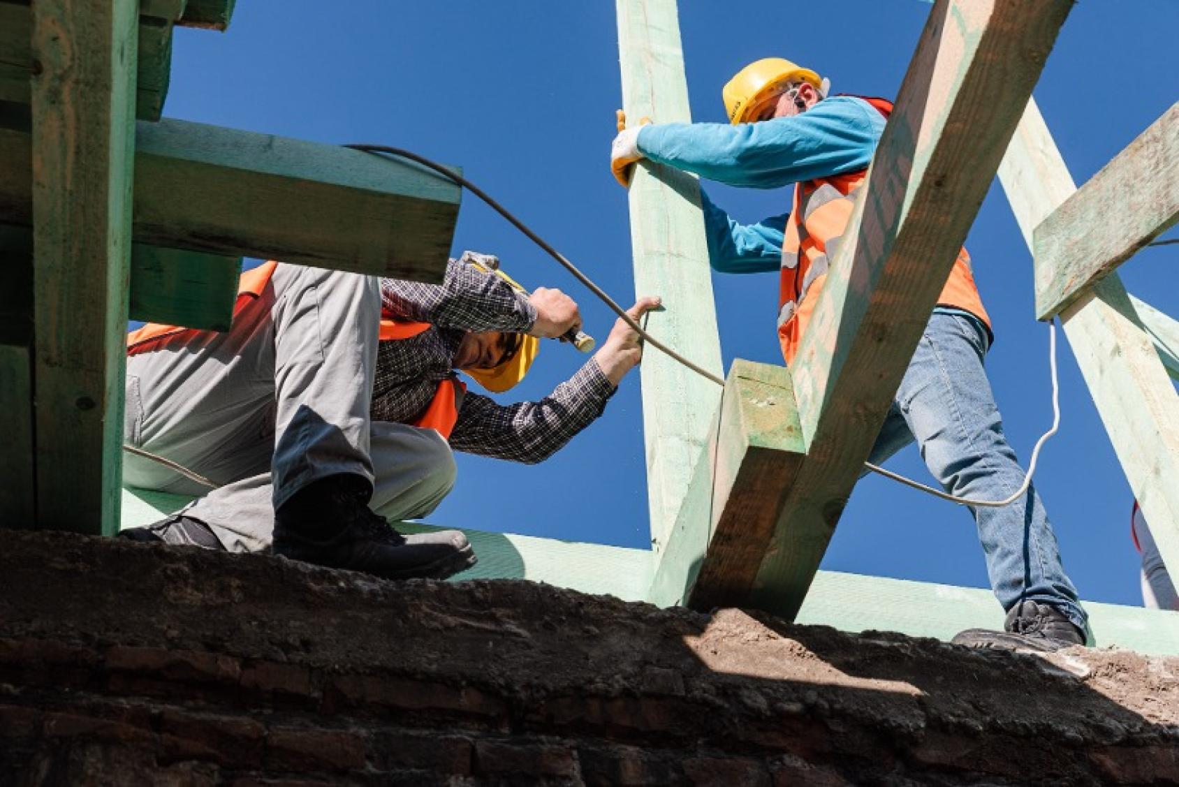 Two men seem to be drilling and hoisting up a pillar in a building under construction.