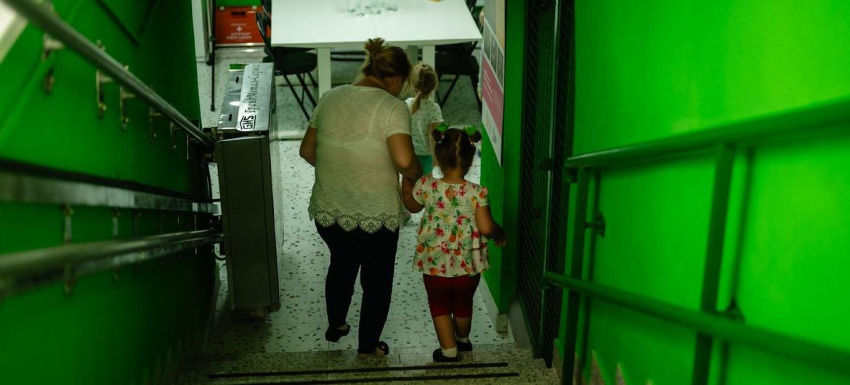 一位大人拉着一个小女孩下楼梯，楼道涂着绿色的油漆。