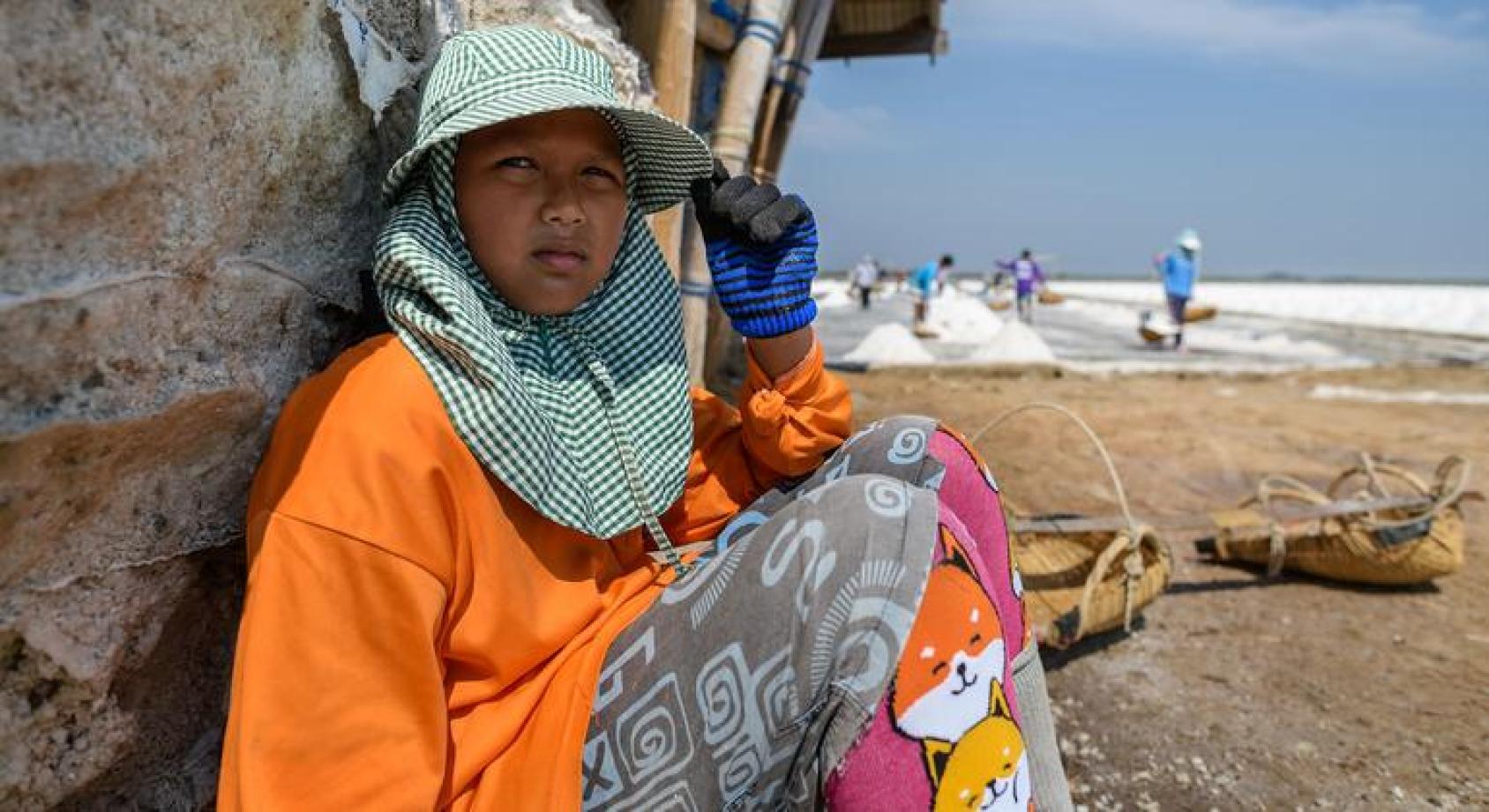 一个孩子坐在疑似沙滩上全副武装戴着帽子和穿着全部包裹的衣服