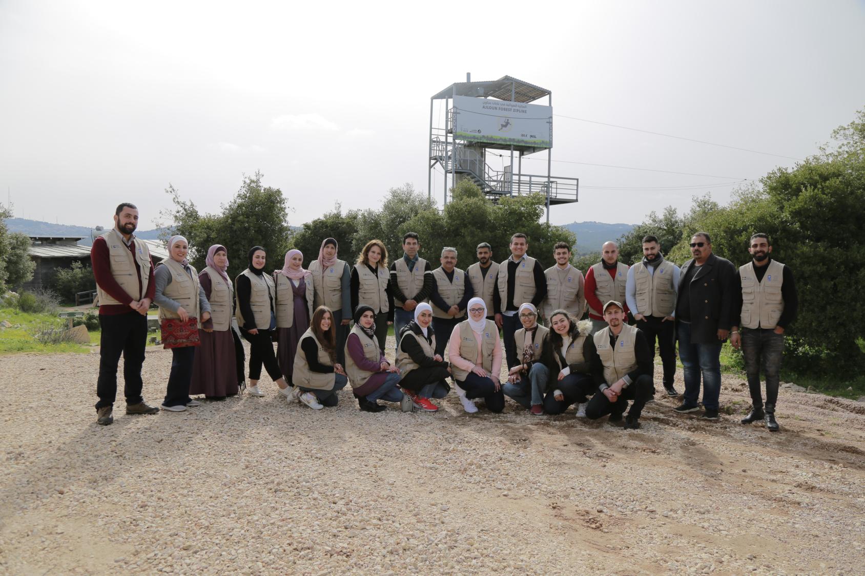 A group of young people in brown uniforms and tan vests take a group photograph together.