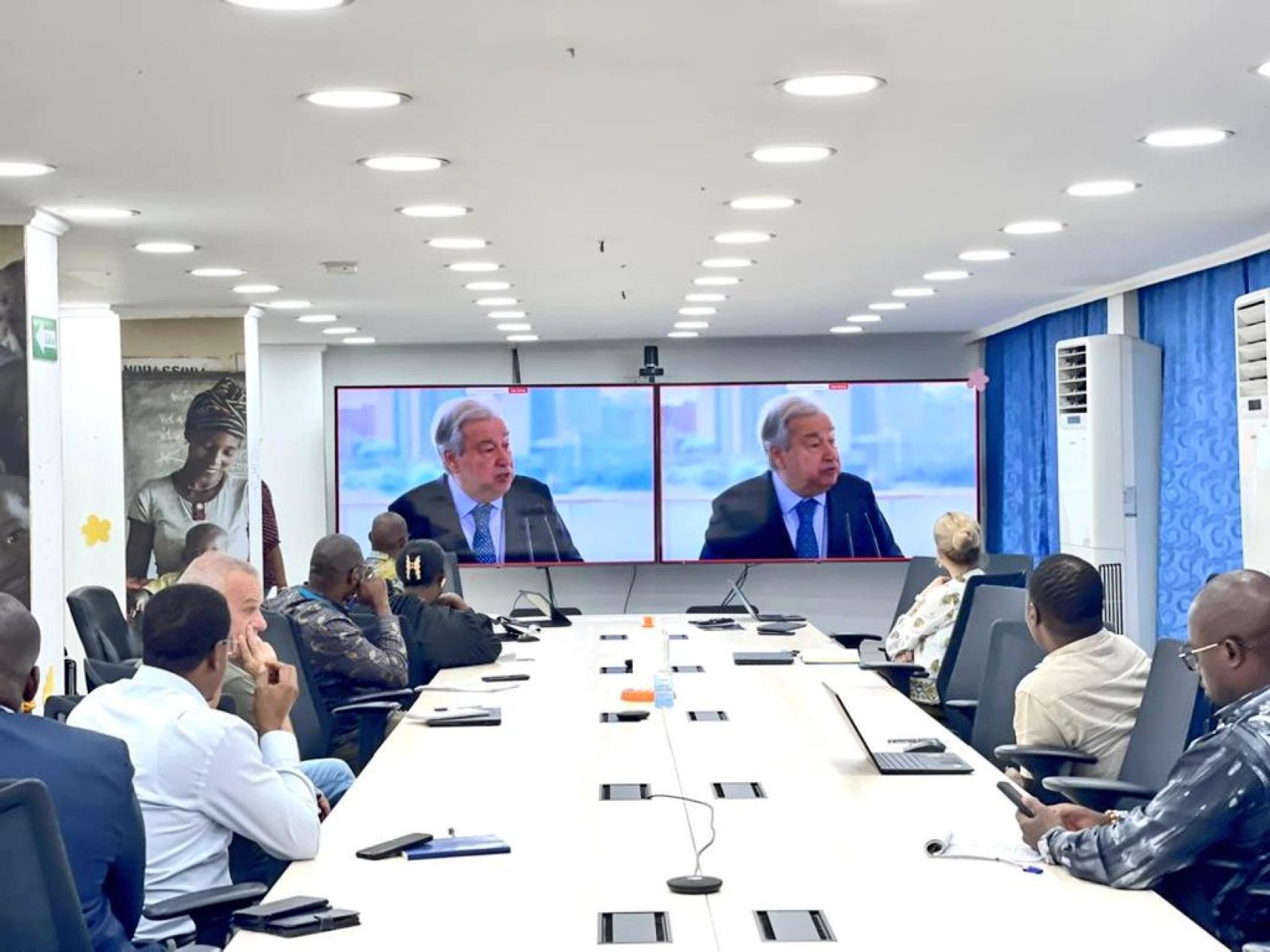 a group of people watching the Secretary-General on a screen