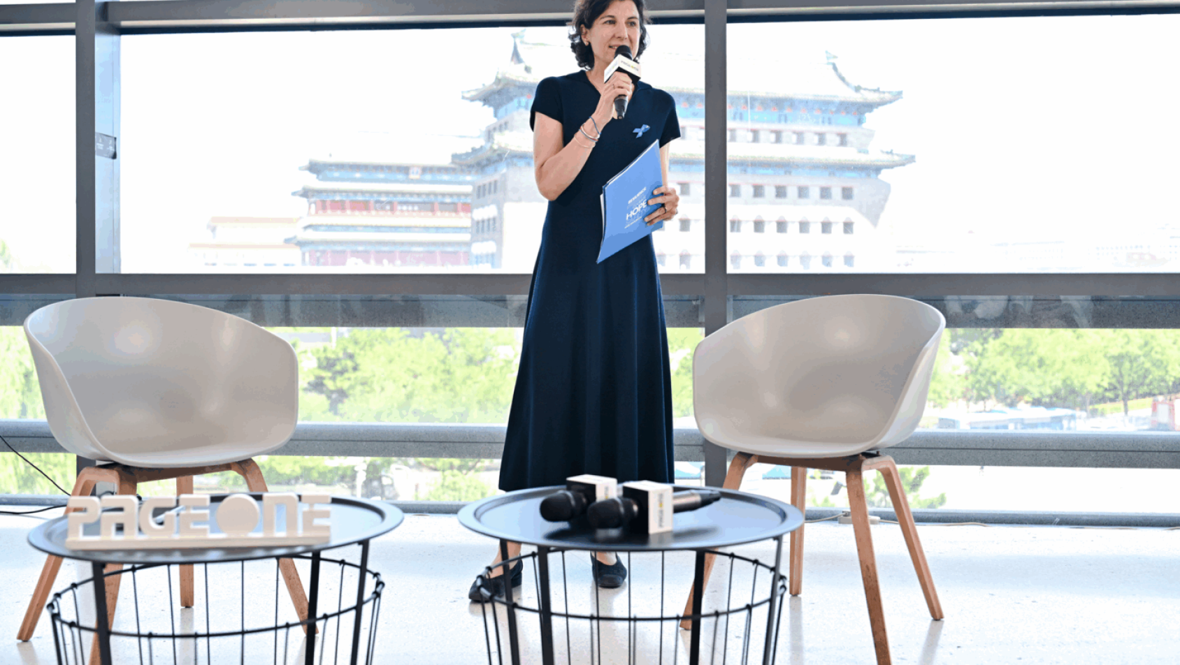 一位身着深色衣服的女性站着拿着话筒发言