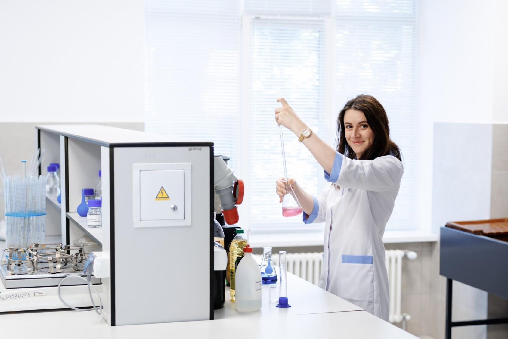 A woman in a lab technician's coat holds out a beaker and a pipette in a laboratory in Moldova