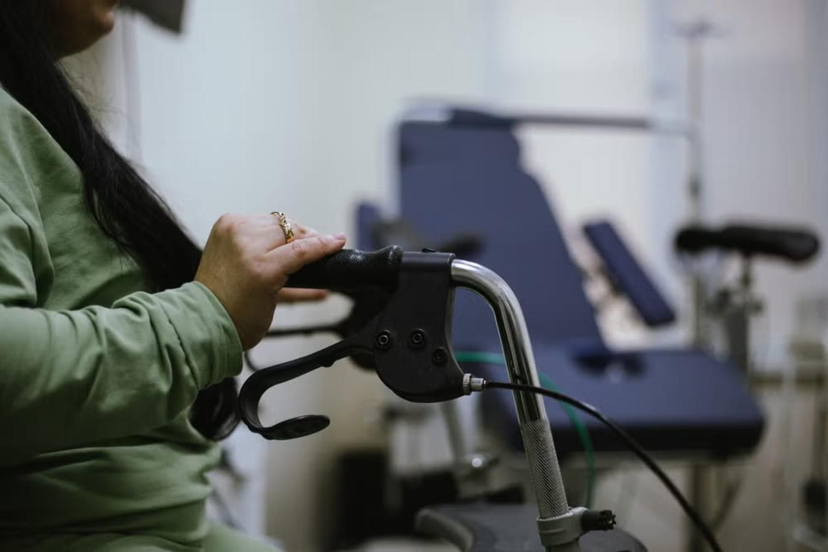 A close-up picture of a woman's hands on a mobility device in a hospital room