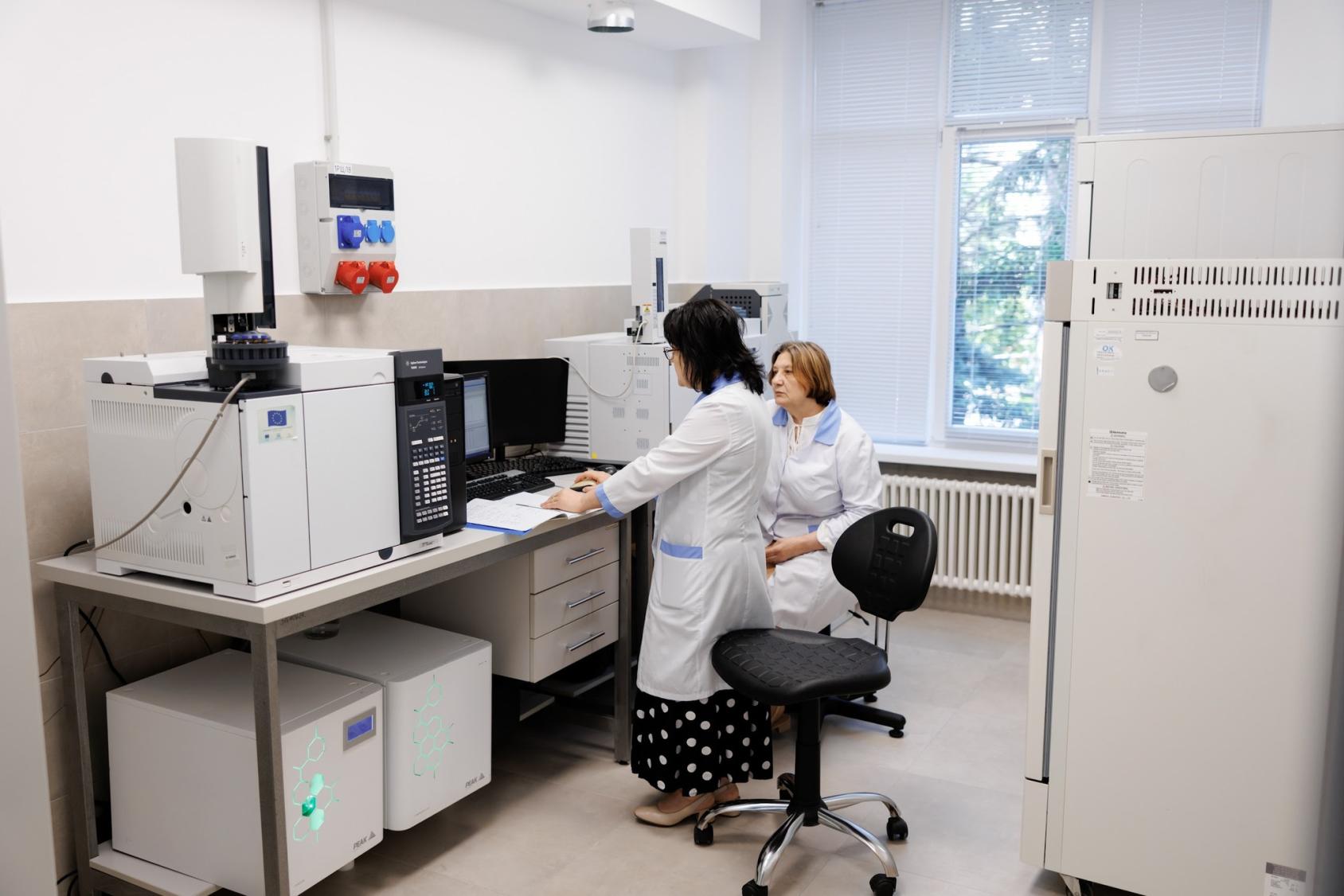 Two women in a laboratory crouched over a machine