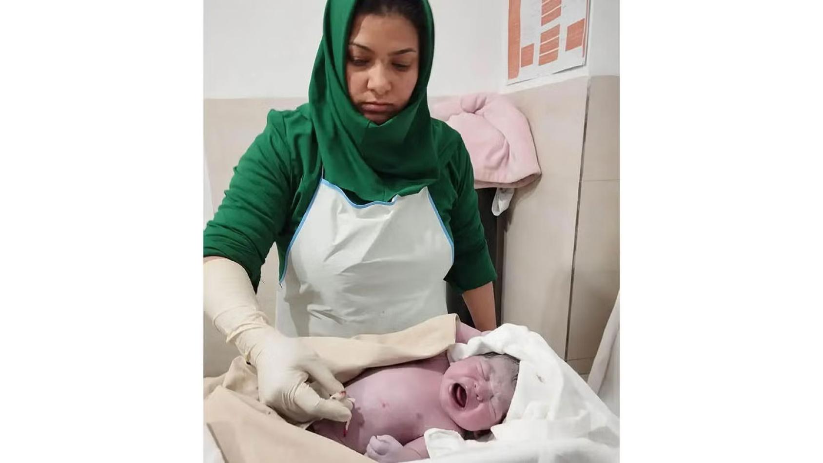 A nurse in a green dress cleans a new born baby that appears to be screaming