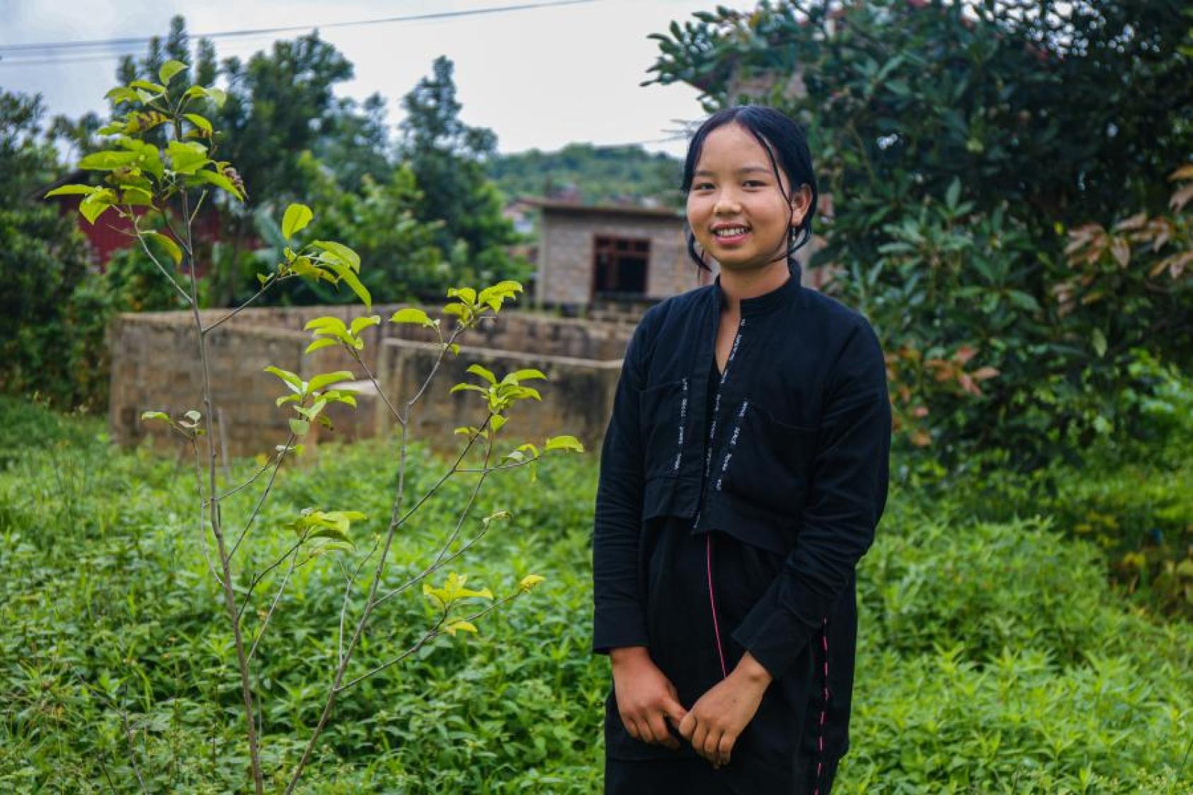 A young woman dressed in black stands in a beautiful garden.