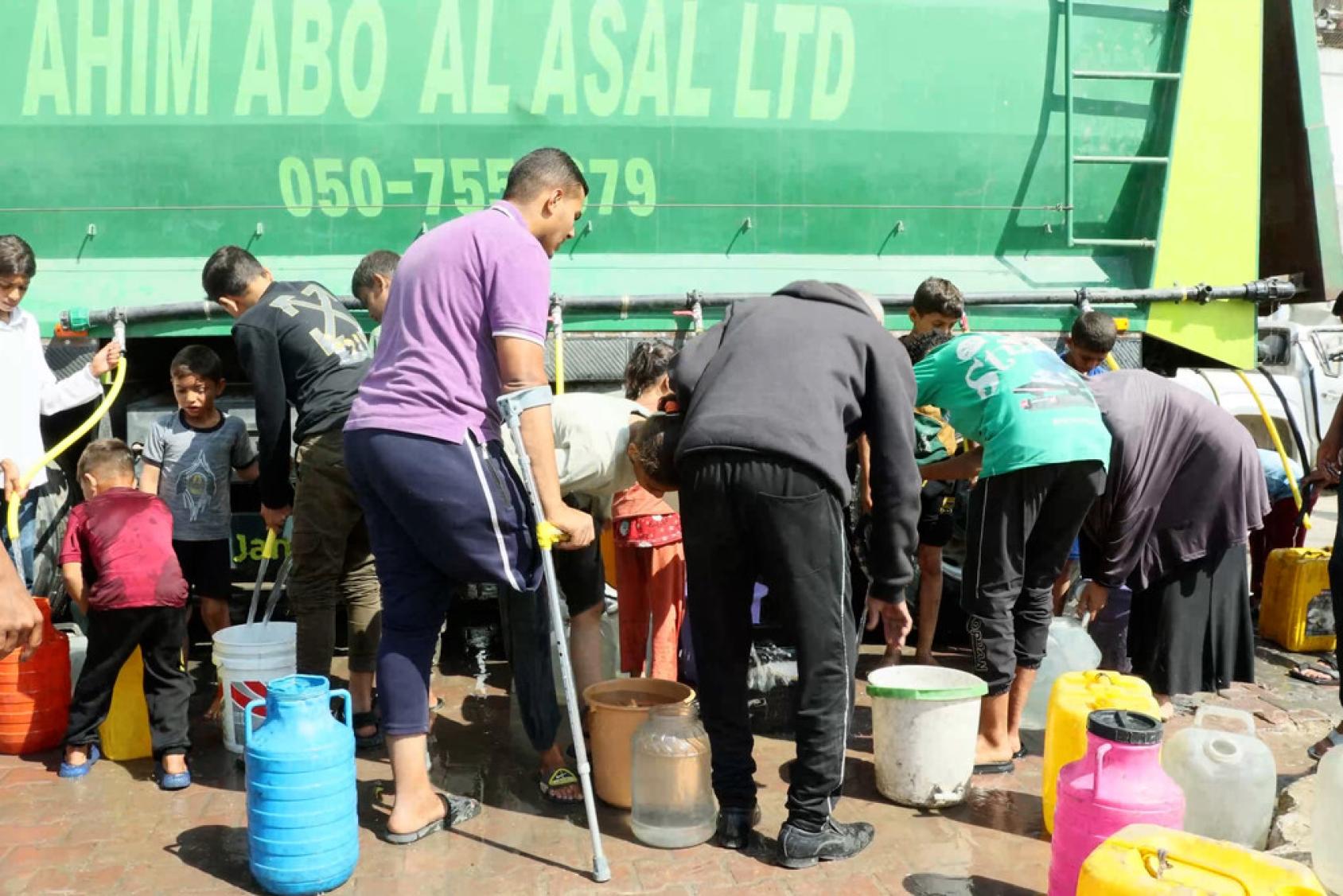 Des personnes se rassemblent pour remplir des récipients avec de l'eau potable provenant d'un camion de distribution du PNUD à Gaza.