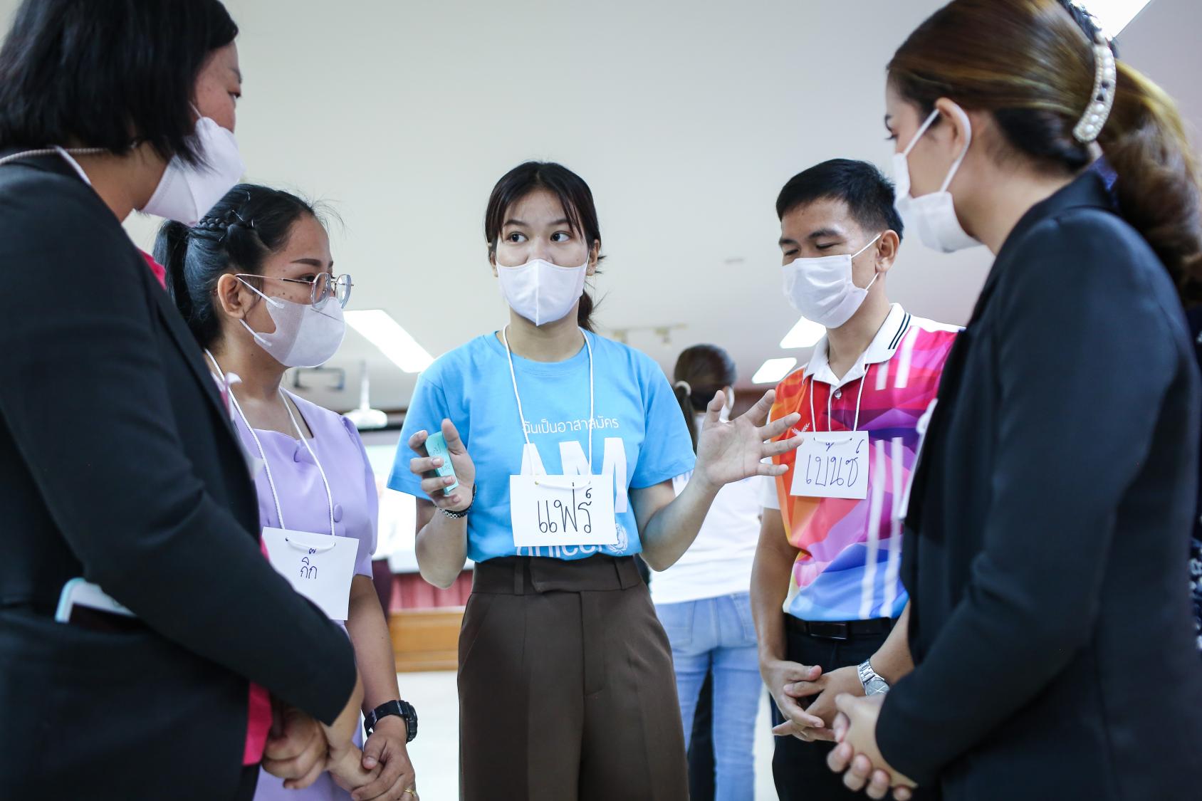 A group of young people in colourful clothes and masks talk amongst each other.