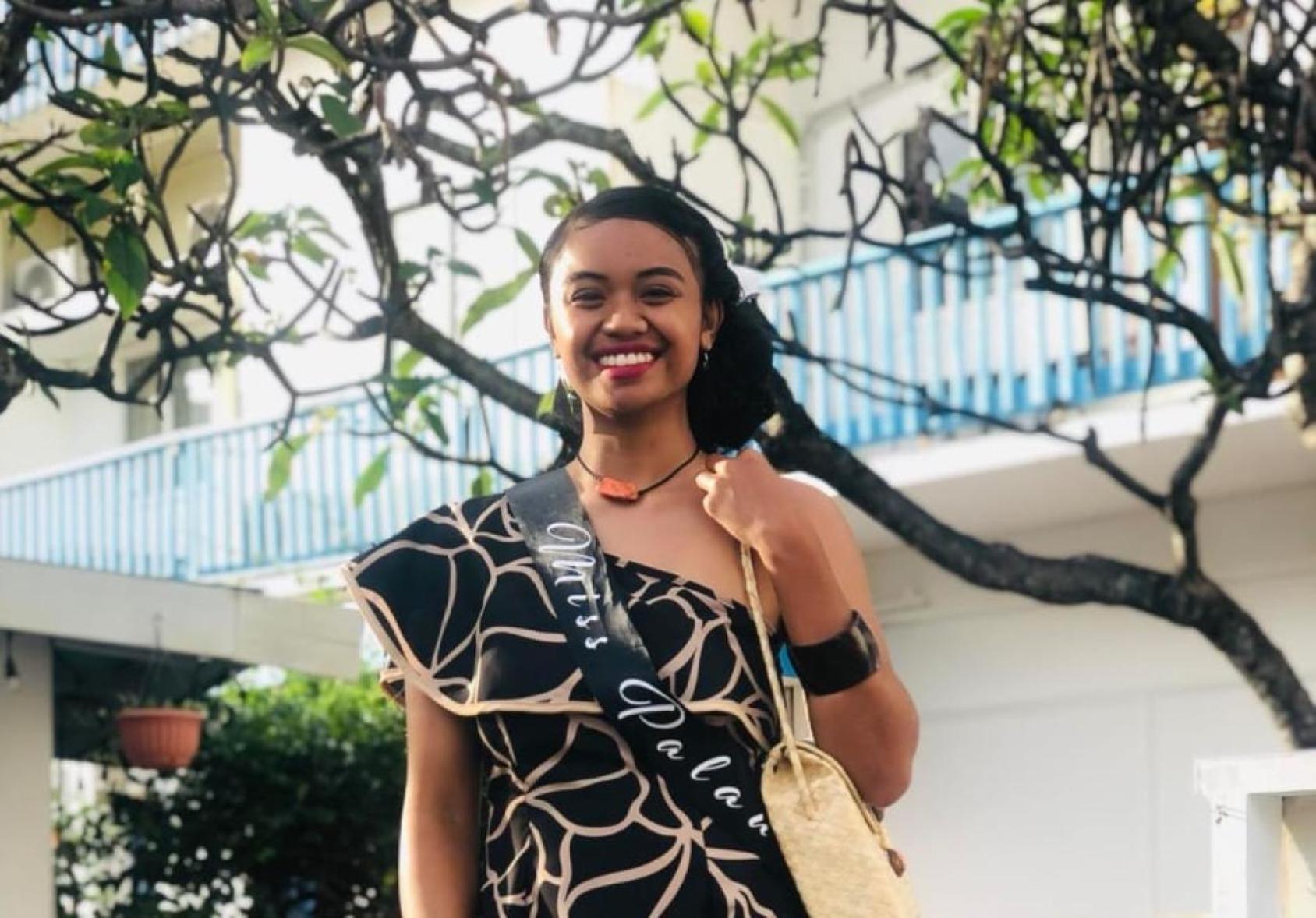 A young woman in a traditional dress stands beneath a tree