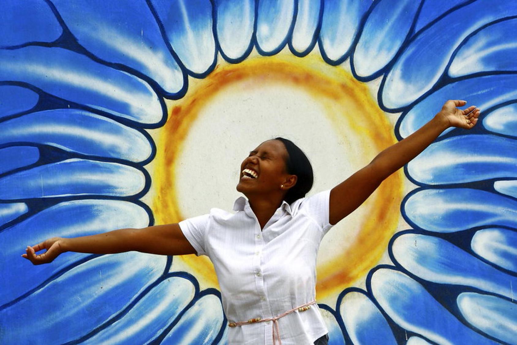 A young Timorese girl stands in front of a mural of a sun.