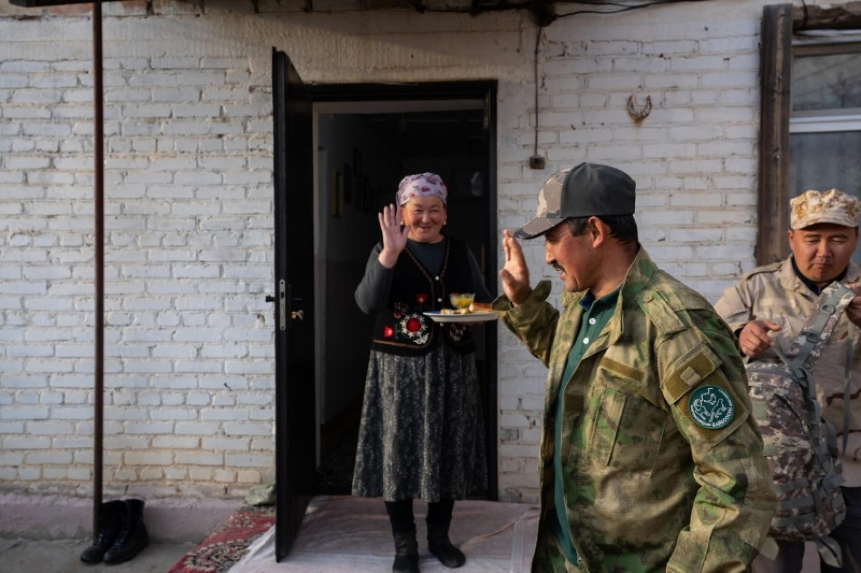 Мужчина машет рукой женщине на пороге дома