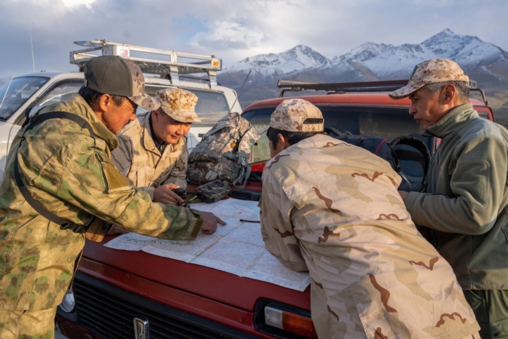 Мужчины стоят у джипа на фоне гор