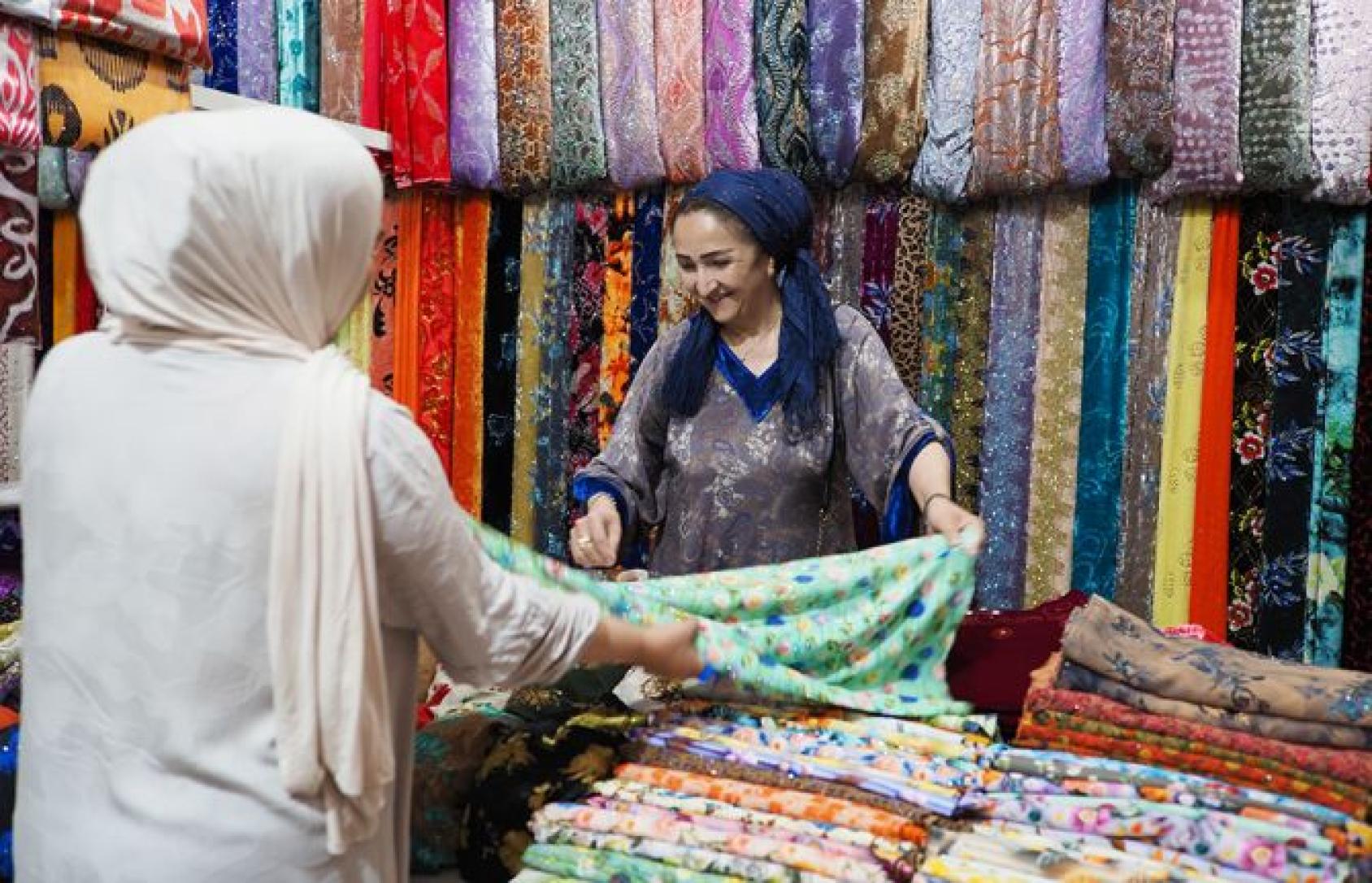 A Tajik woman shows a shawl to another woman.