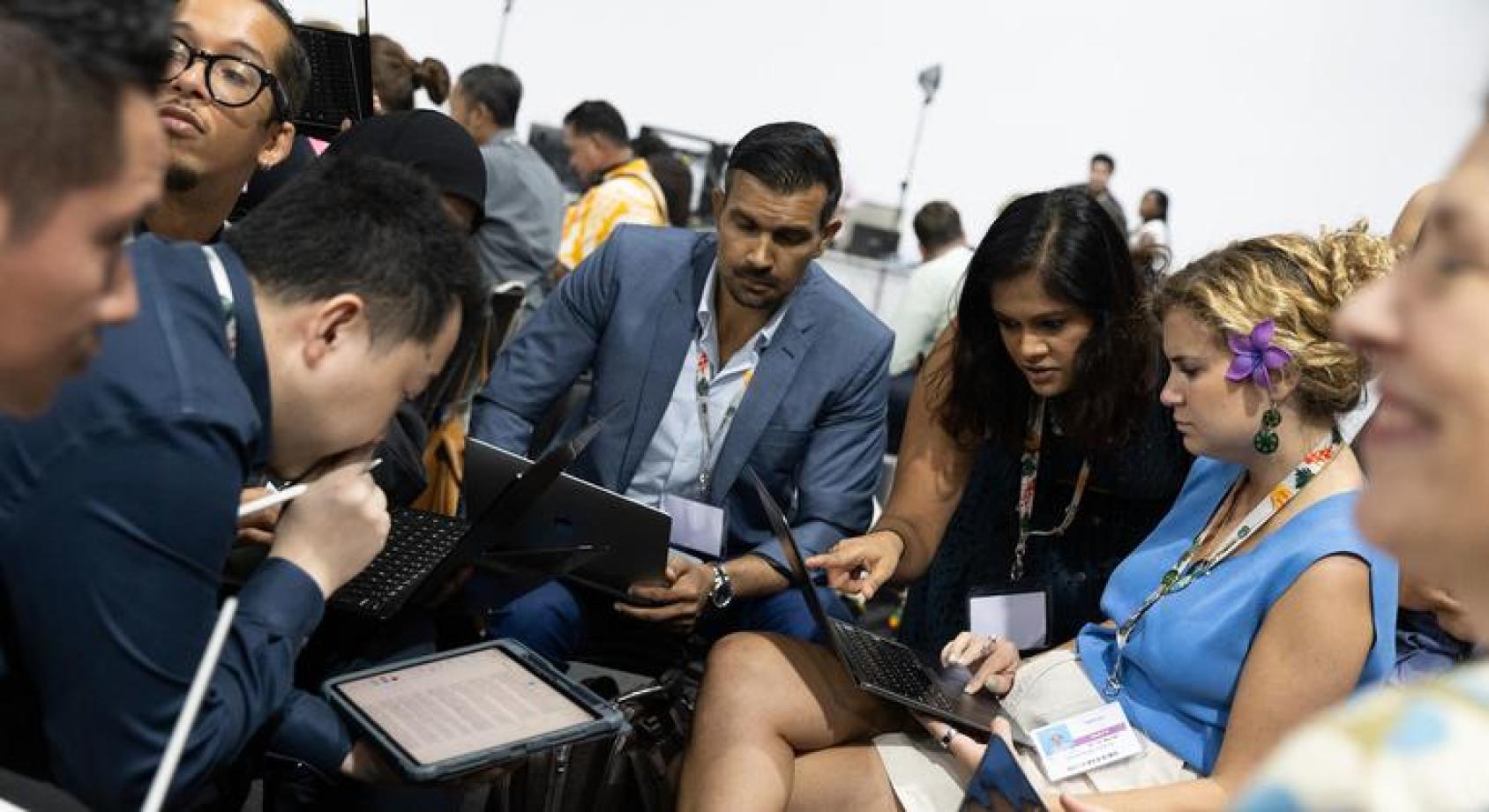 一群人围坐在电脑等手持电子设备前写东西看东西