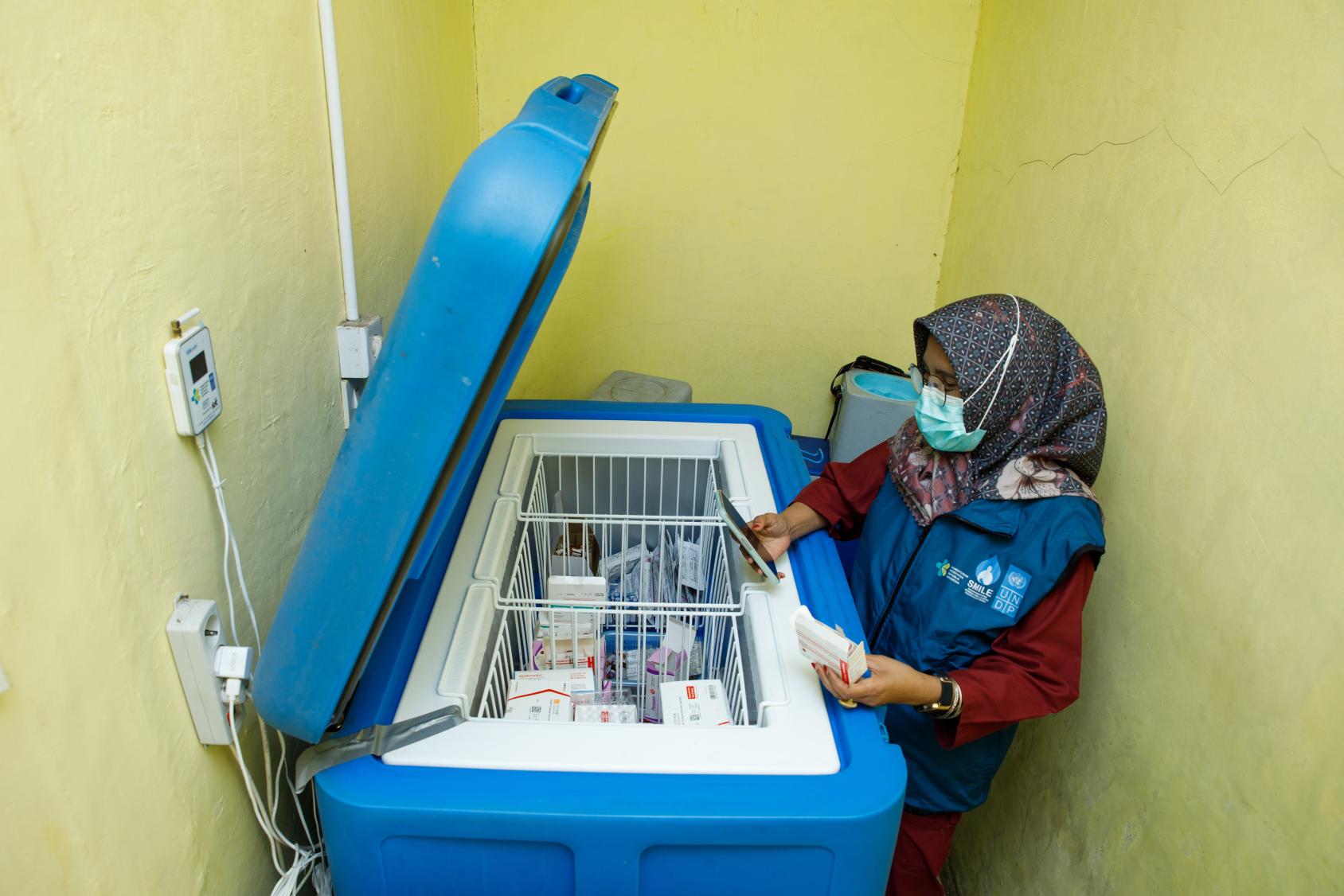 A woman in Indonesia looks over a large container of vaccines and medical supplies.