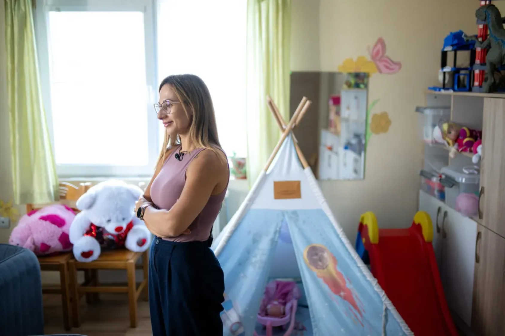 Девушка стоит в детской комнате, скрестив руки