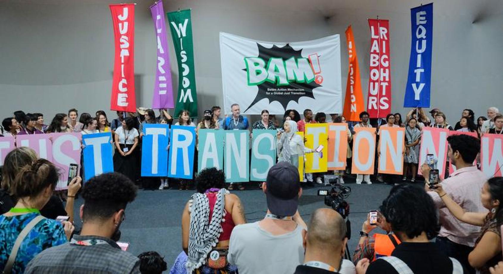 一群人举着巨大的字母排列成一排，其中当中的字母拼成的单词是TRANSITION