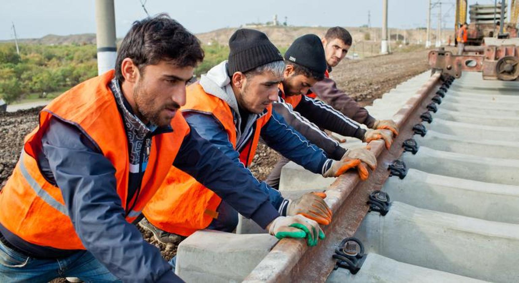 几名工人身穿蓝色制服外面套着橙色反光马甲，正在修建铁路