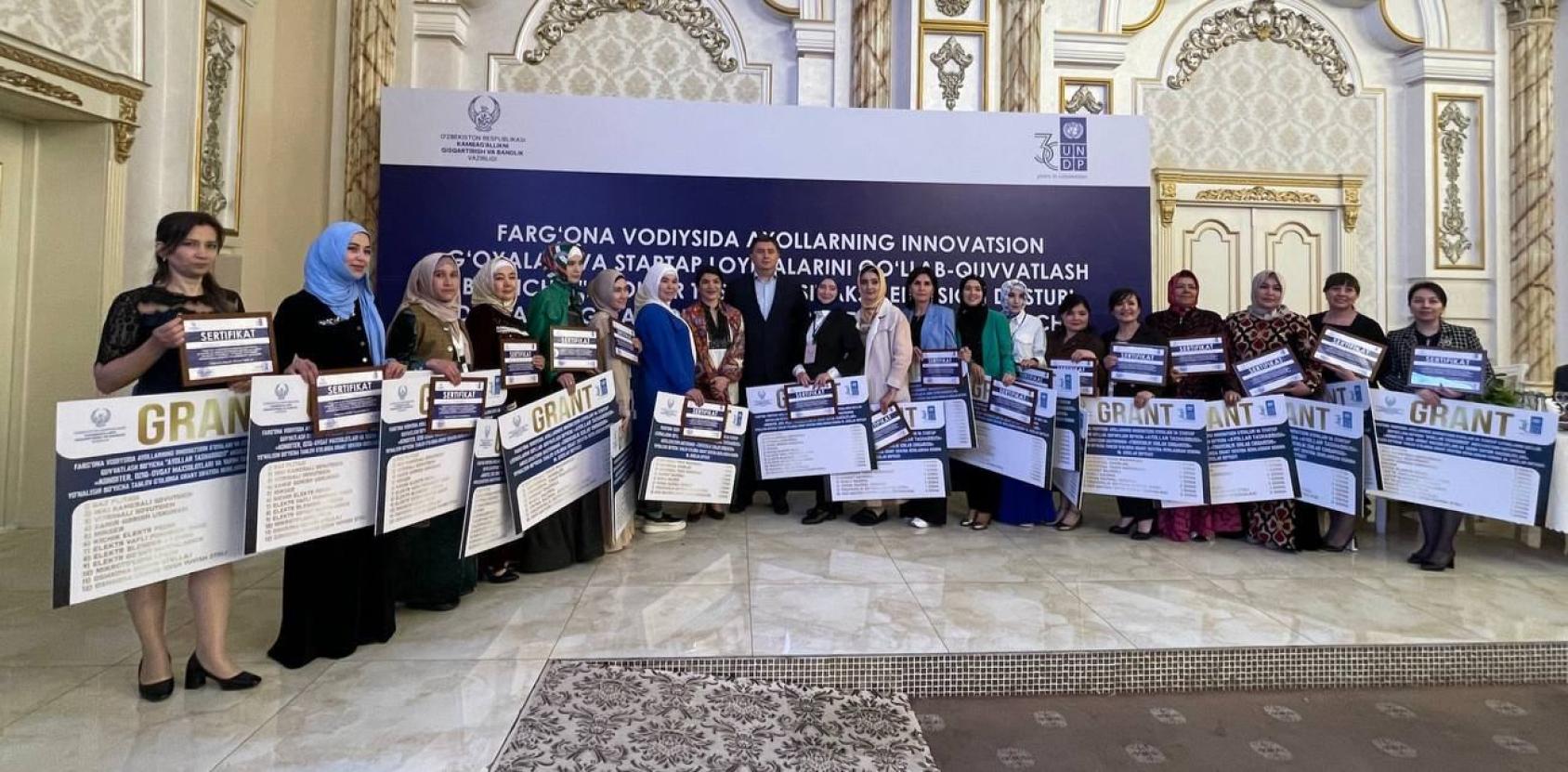 Женщины стоят с большими сертификатами в руках в украшенном зале