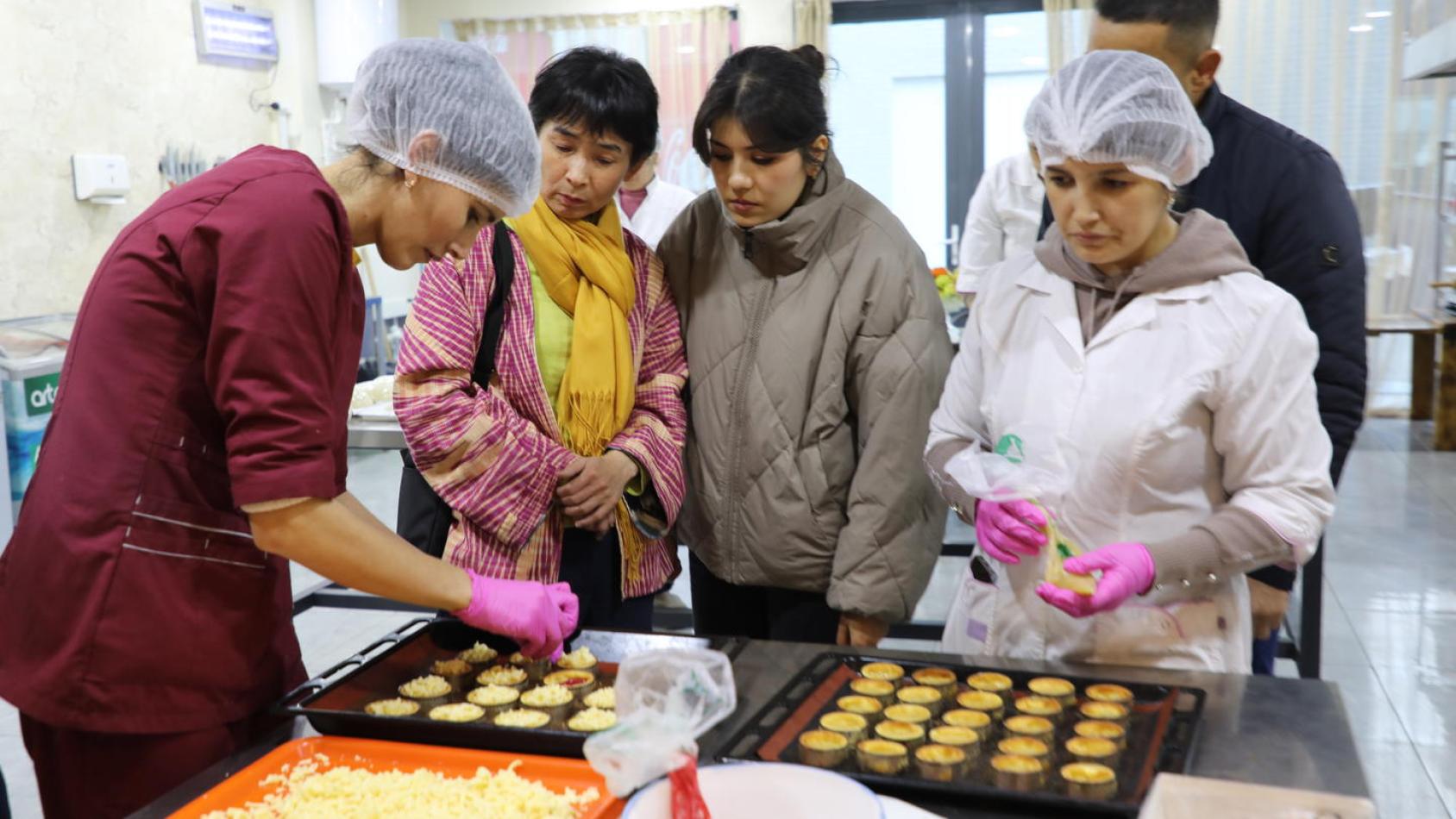 Группа людей украшает небольшие десерты в учебном кабинете для занятий кулинарией.